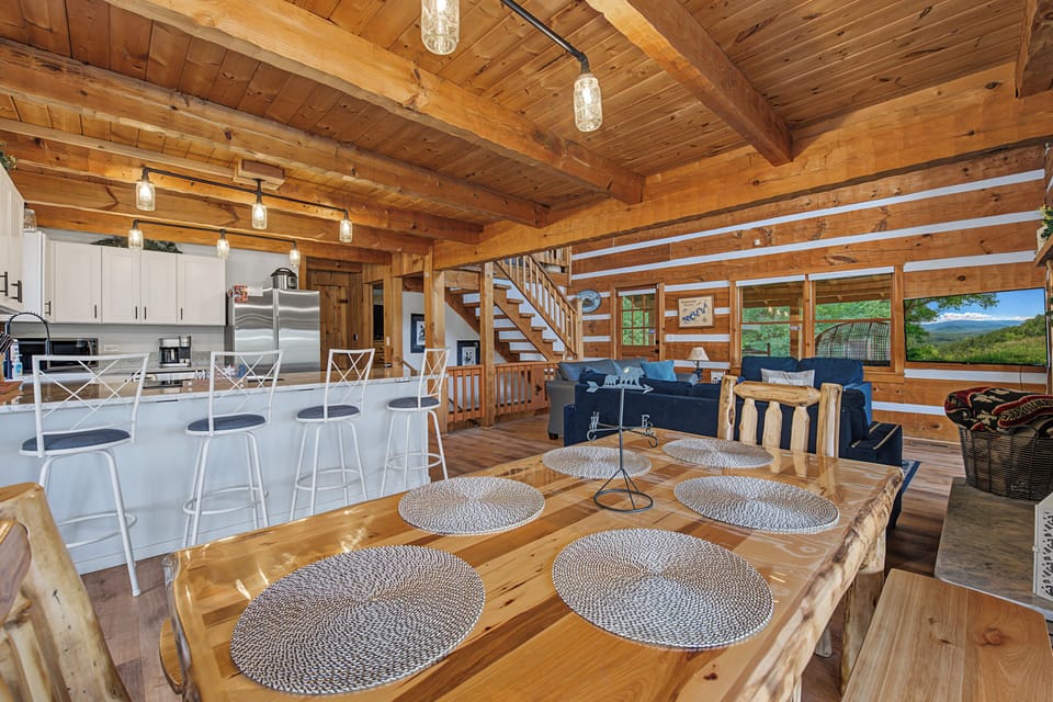 Gather around the handcrafted dining table and soak in mountain views through expansive windows. This open-concept retreat blends rustic wood beams with modern comforts, perfect for memorable meals and cozy evenings together.