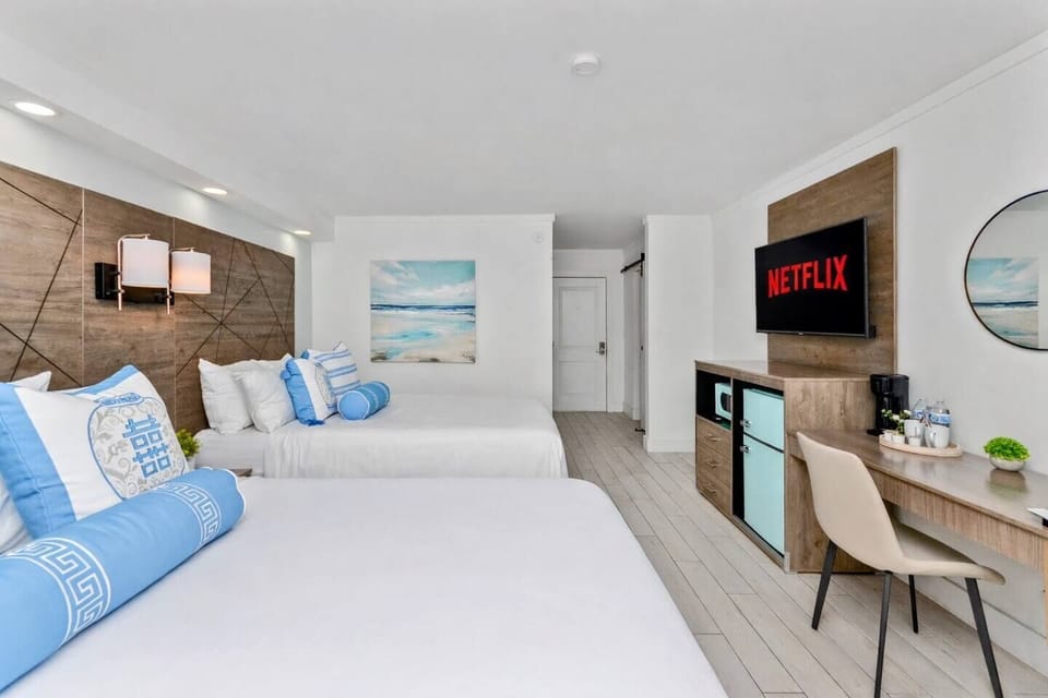Bright, modern bedroom with two cozy queen beds, stylish wood accent wall, soft linens, bedside lighting, and blackout shade—perfect for a restful stay.