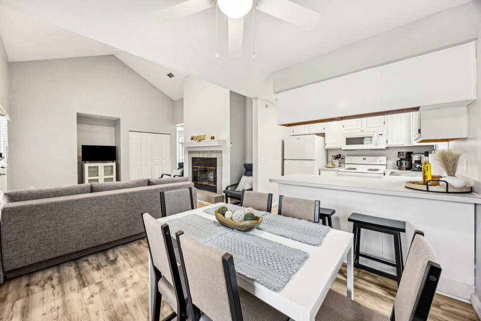 Your bright open-concept space seamlessly blends kitchen, dining, and living areas under soaring vaulted ceilings with cozy fireplace warmth.