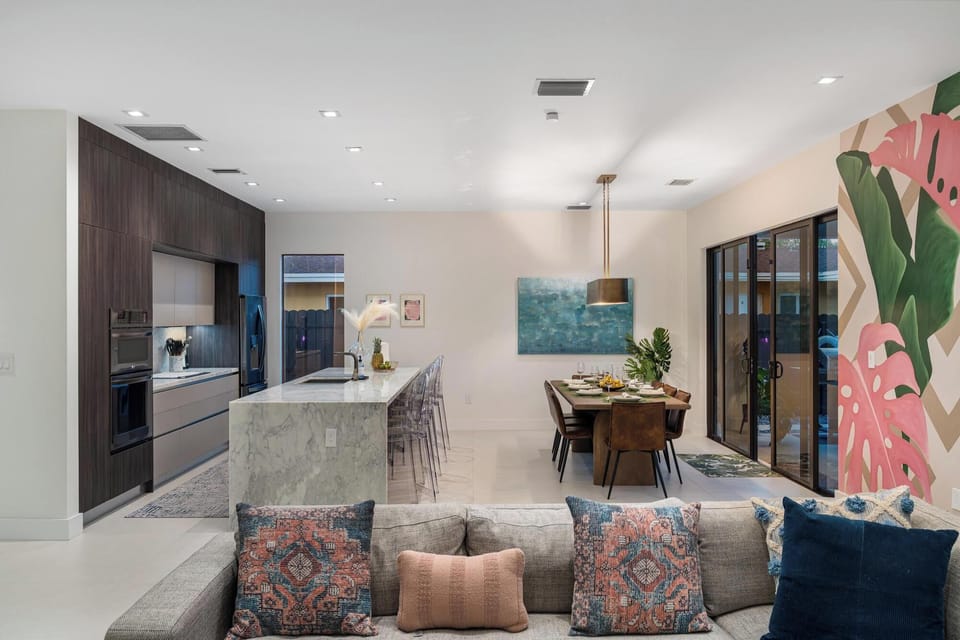 
Open concept living room and dining room with Casa Monstera mural. Large sliding glass doors open up to back patio and pool deck.
