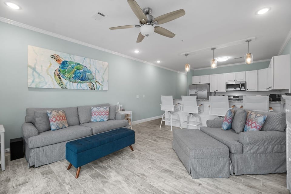 Open-concept living and dining area at Pescador Landing, Perdido Key – sea turtle wall art, plush sectional sofa, and views to the kitchen. A coastal oasis near FloridaBama.