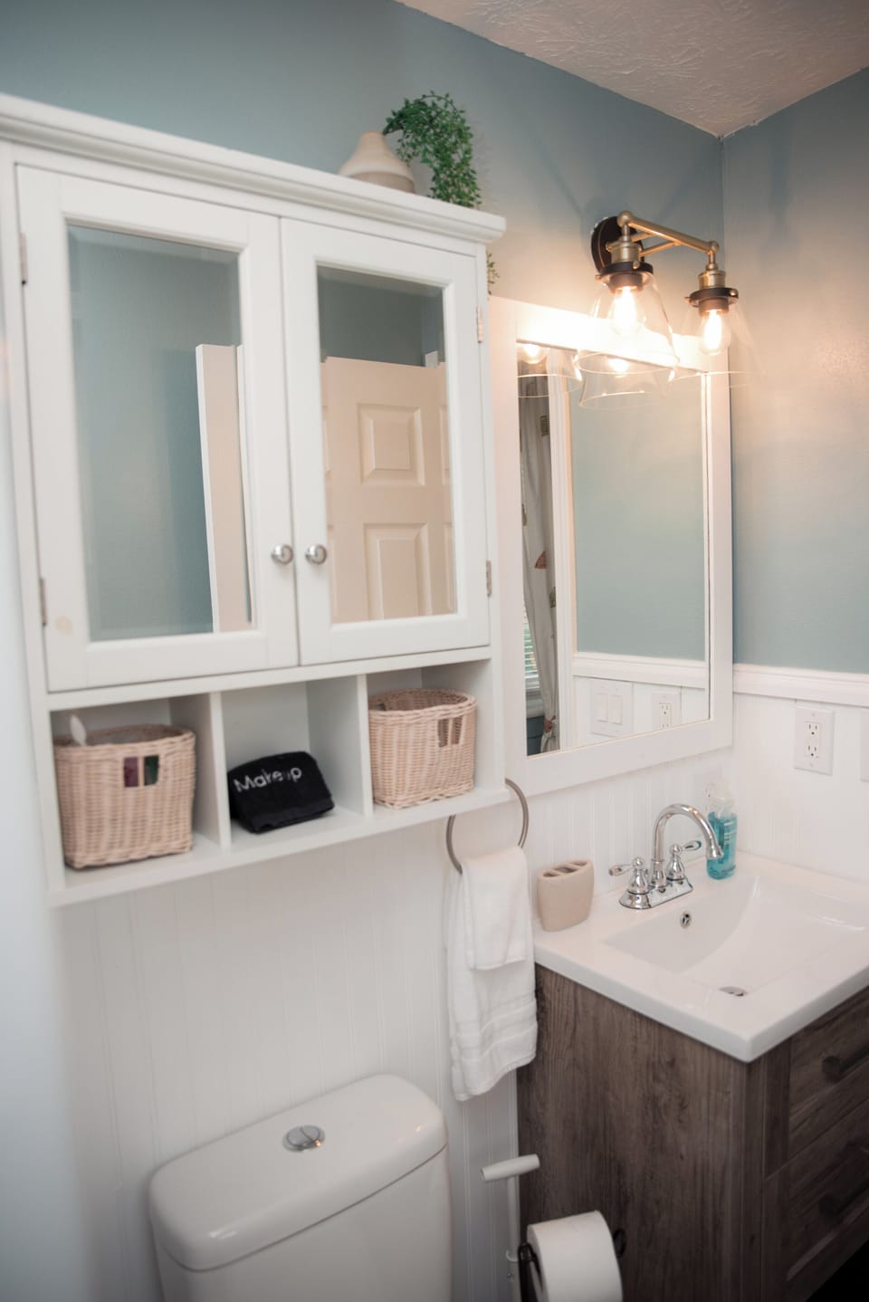 Modern vanity with bright lighting and organized storage using wicker baskets.