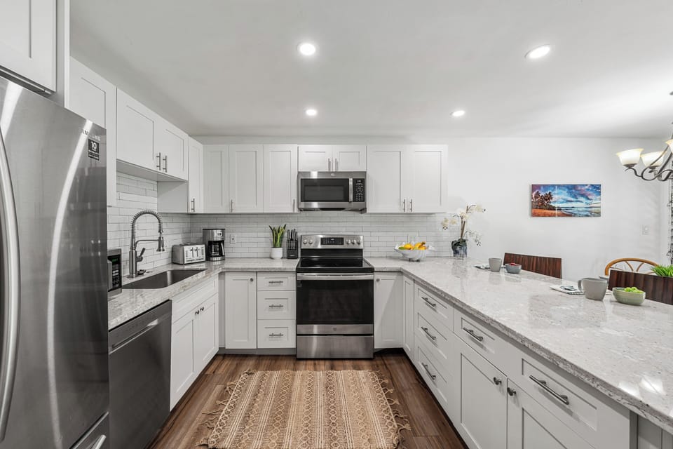 Fully equipped kitchen featuring stainless steel appliances, white cabinetry, and bar seating for three.