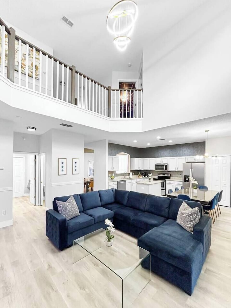 Luxurious open-concept living room with soaring tall ceilings, a plush sectional that turns into a sleeper, and modern statement lighting. This bright, spacious lounge flows effortlessly into the kitchen dining area- ideal for family gatherings.