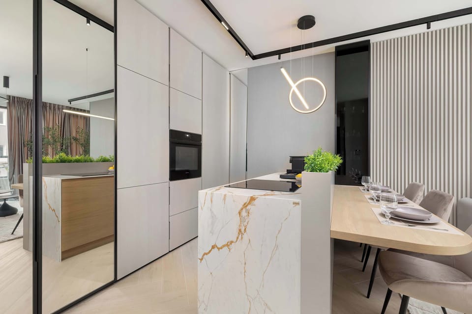 A dining area connected to the kitchen, featuring a marble-style table and modern chairs. Glass partitions separate zones while keeping the space open. Soft lighting enhances the elegant feel.