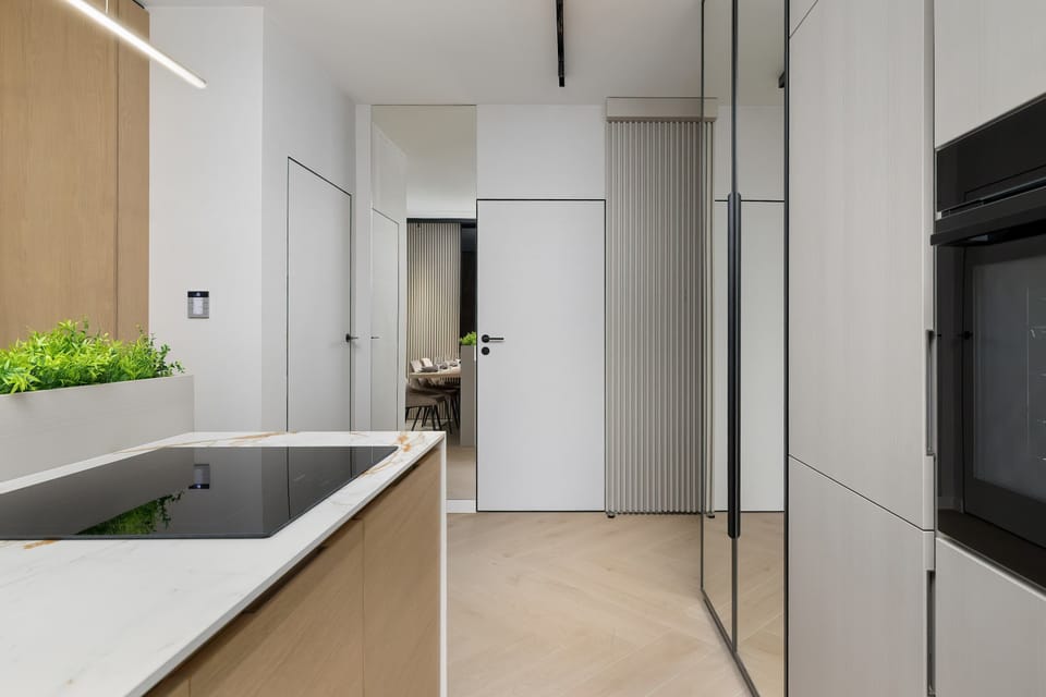 A hallway view with built-in storage and a clean tiled floor. Light walls and concealed doors create a seamless look. The corridor feels spacious and uncluttered.