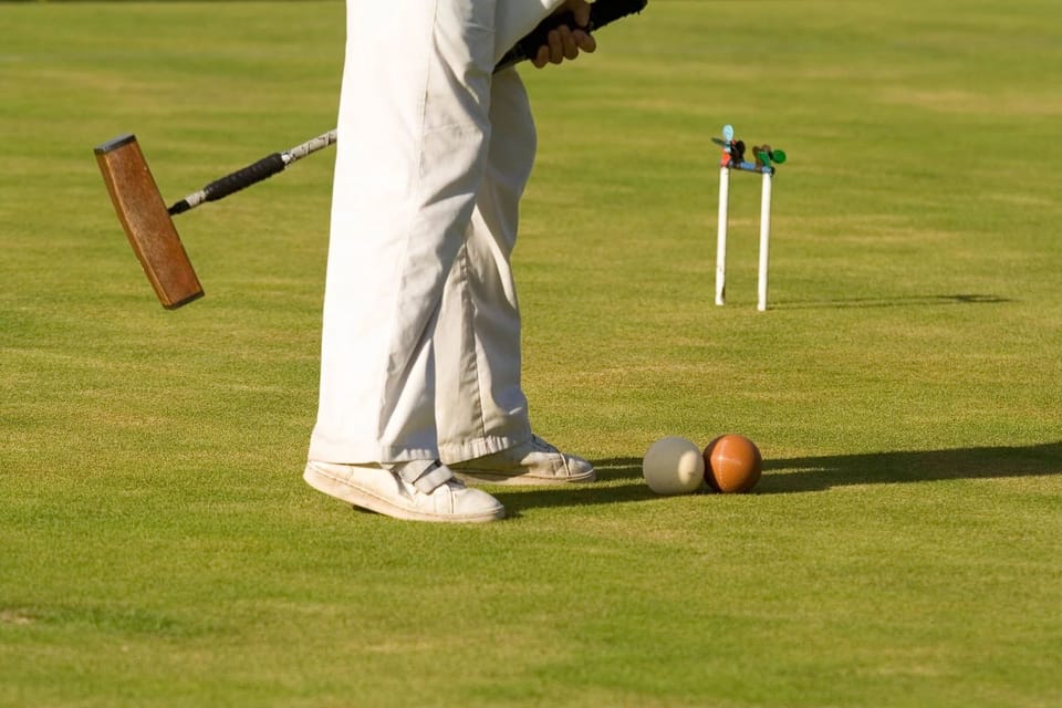 A focused moment in croquet, capturing a player poised to strike the ball on a perfectly manicured lawn, exemplifying leisure elegance.