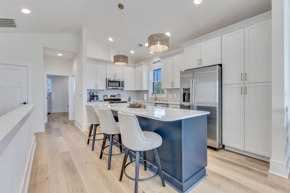 Your modern kitchen awaits with sleek white cabinets, gleaming quartz counters, and a striking blue island perfect for morning coffee.