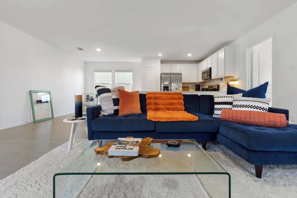 Spacious living room with a cozy navy sectional, bright natural light, and a 55” TV for streaming your favorite shows. This open-concept space flows into the kitchen and dining areas, creating the perfect place to unwind, gather, and relax.