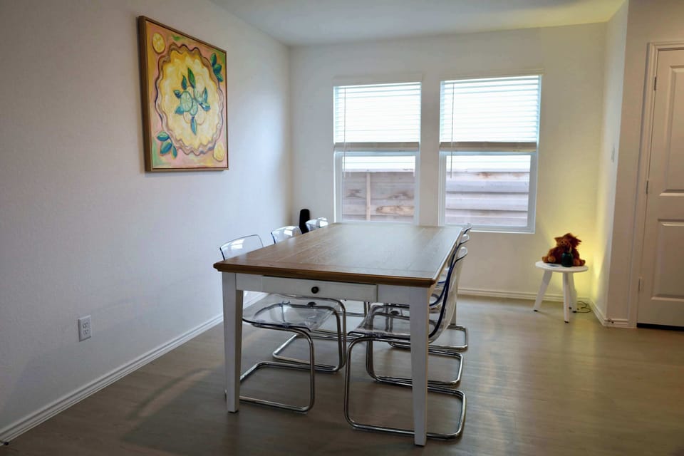 Bright kitchen and dining area featuring stainless-steel appliances, wide countertops, and a modern round table overlooking the backyard. The open layout flows into the living room, where a 55” TV creates the perfect place to relax after meals.