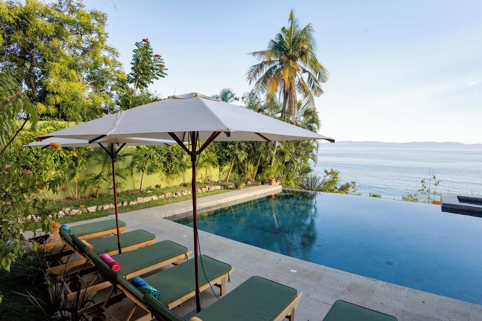 Infinity pool overlooking the ocean, surrounded by lush greenery and a spacious lounge area—perfect for relaxing, sunbathing, and enjoying the view.