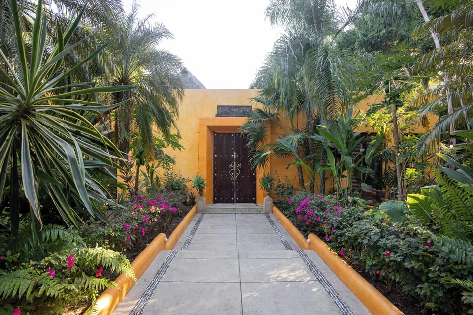 Lush garden walkway leading to the main entrance, surrounded by tropical plants and vibrant greenery.