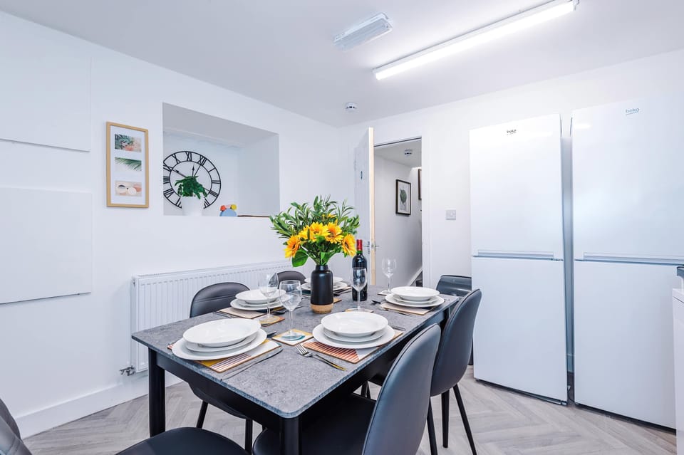 Bright, modern kitchen highlights the dining area alongside tall white units and a freestanding fridge freezer. Modern finishes, bright lighting, and clean lines create a practical and well-designed kitchen-dining space.