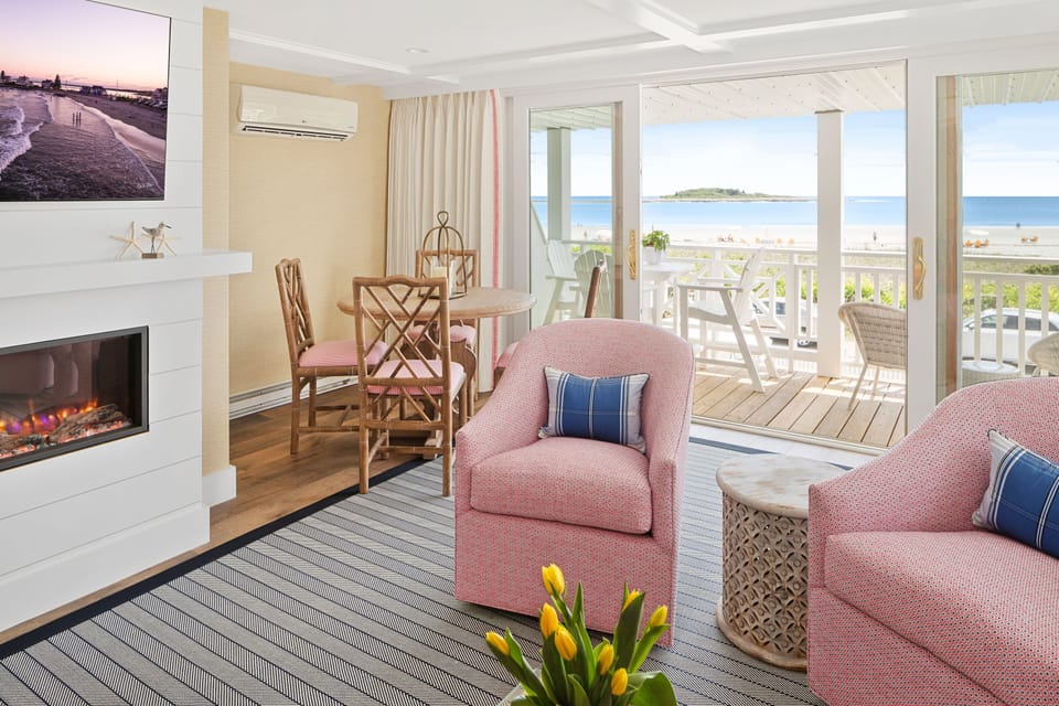 The bright and airy living space features cozy seating, a dining area, and breathtaking views of Goose Rocks Beach through expansive glass doors.