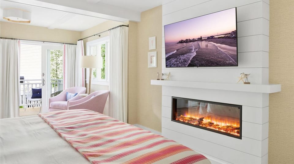 This serene bedroom is elegantly appointed with inviting decor, a cozy fireplace, and doors leading to a lovely outdoor space, ideal for unwinding after a day at the beach.
