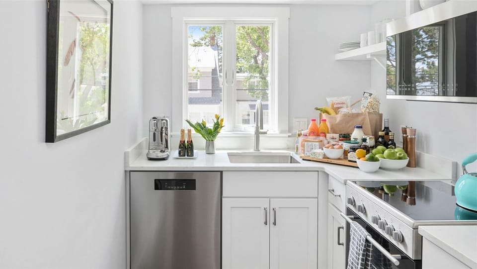 This modern kitchen boasts a sleek design with ample storage, a sunny window, and a variety of beverages and fresh ingredients ready for your culinary adventures.