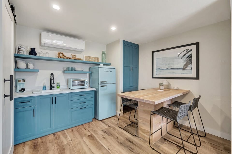 Bright dining nook w/ wood table, open shelving & blue cabinetry for casual meals