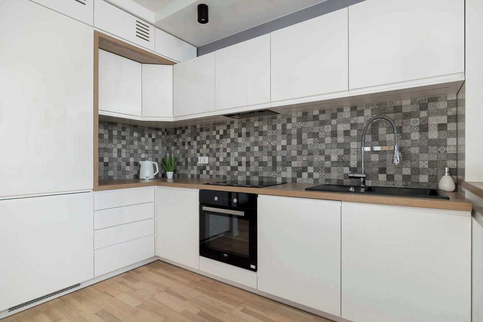 A corner view of the kitchen highlighting the patterned backsplash and oven. White cabinetry and wood accents balance warmth and simplicity. The layout feels compact yet efficient.