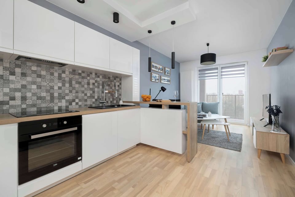 A wide kitchen shot with ample counter space and integrated appliances. Light wood flooring adds warmth to the otherwise white interior. The space looks bright and airy.