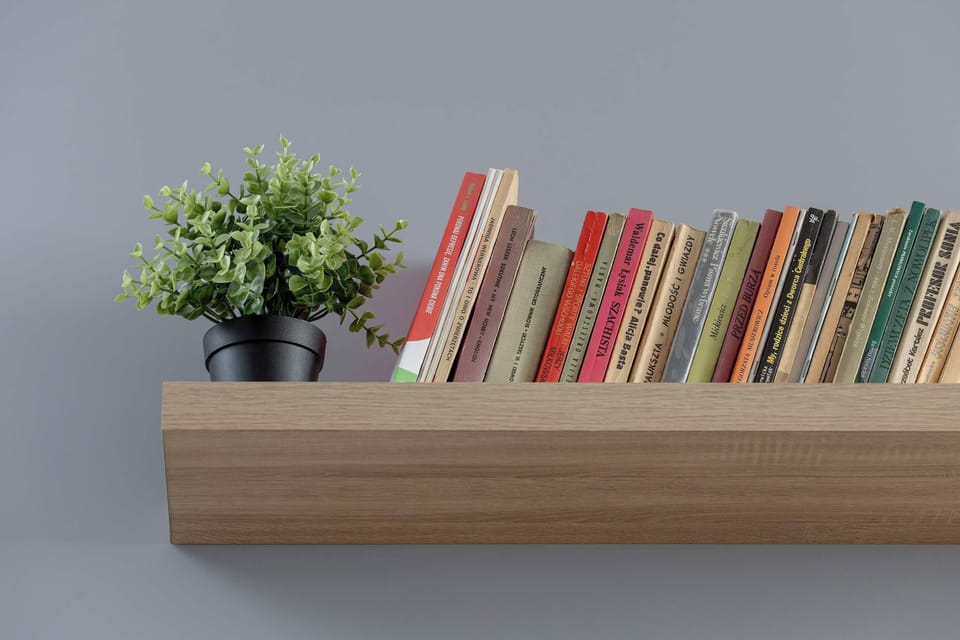 A close-up of a wall shelf holding colorful books and a small plant. The decor adds personality and color to the interior. The shelf is neatly arranged.