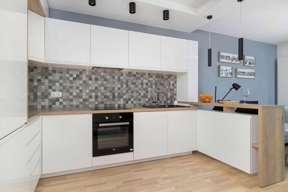 A modern kitchen with white cabinets, patterned backsplash tiles, and built-in appliances. The clean lines and light finishes create a fresh look. The space appears well-organized and practical.