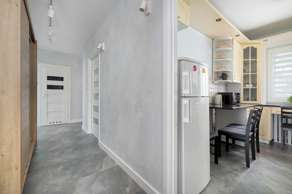 Hallway leading to the kitchen, with gray tiles and bright walls. Functional layout with natural light from the adjacent room.