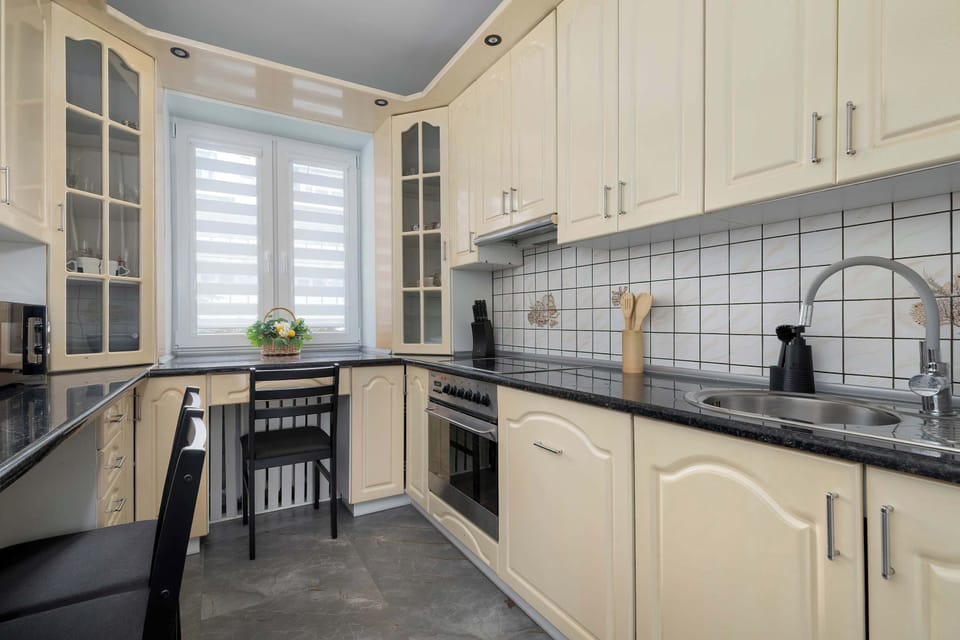 Kitchen with cream cabinets, black countertops, and dining area. Modern appliances and window providing daylight.