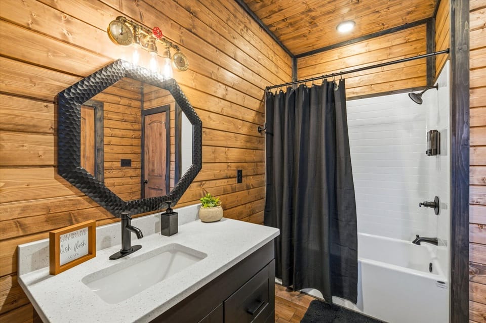 Rustic bathroom with octagonal mirror, dark vanity, and industrial mountain charm.