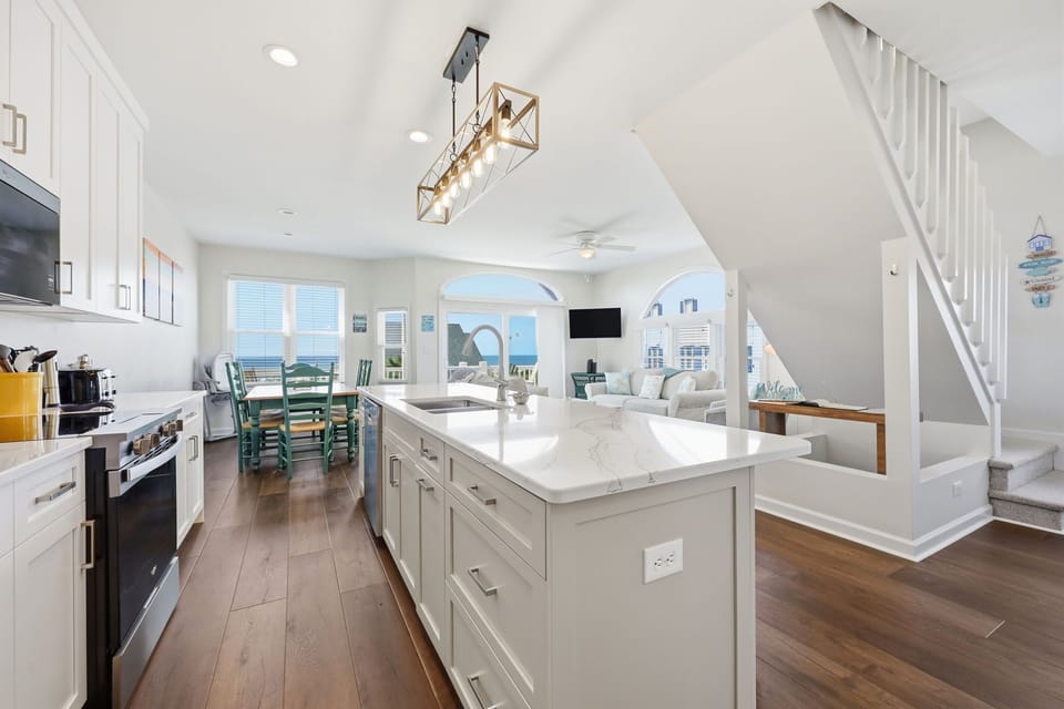 Your open-concept living space flows seamlessly from a chef's kitchen with marble countertops to a bright living area, all framed by stunning ocean views through arched windows.