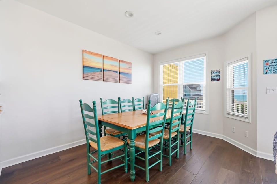 Gather around this inviting dining table with seating for eight, where sunlight and coastal breezes stream through large windows showcasing views of the surrounding area.