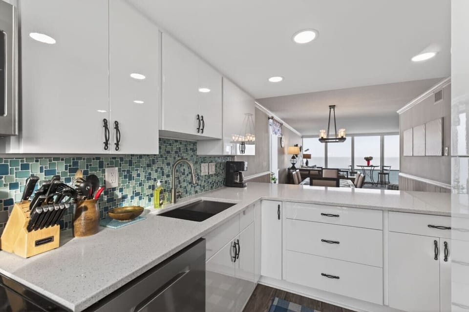 Bright, modern kitchen with white cabinetry, updated appliances, and stylish tile backsplash. Open layout flows into the dining and living areas, making it easy to cook, gather, and enjoy oceanfront living.