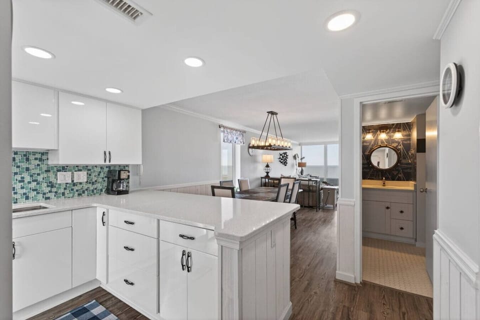 Spacious, updated kitchen with bright white cabinetry and ample counter space. Open layout leads to the dining and living areas, with easy access to a stylish bathroom, perfect for comfortable coastal stays.