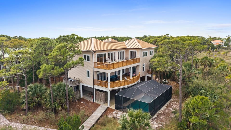 Modern three-story beach house with wraparound decks nestled among coastal palms and native vegetation.