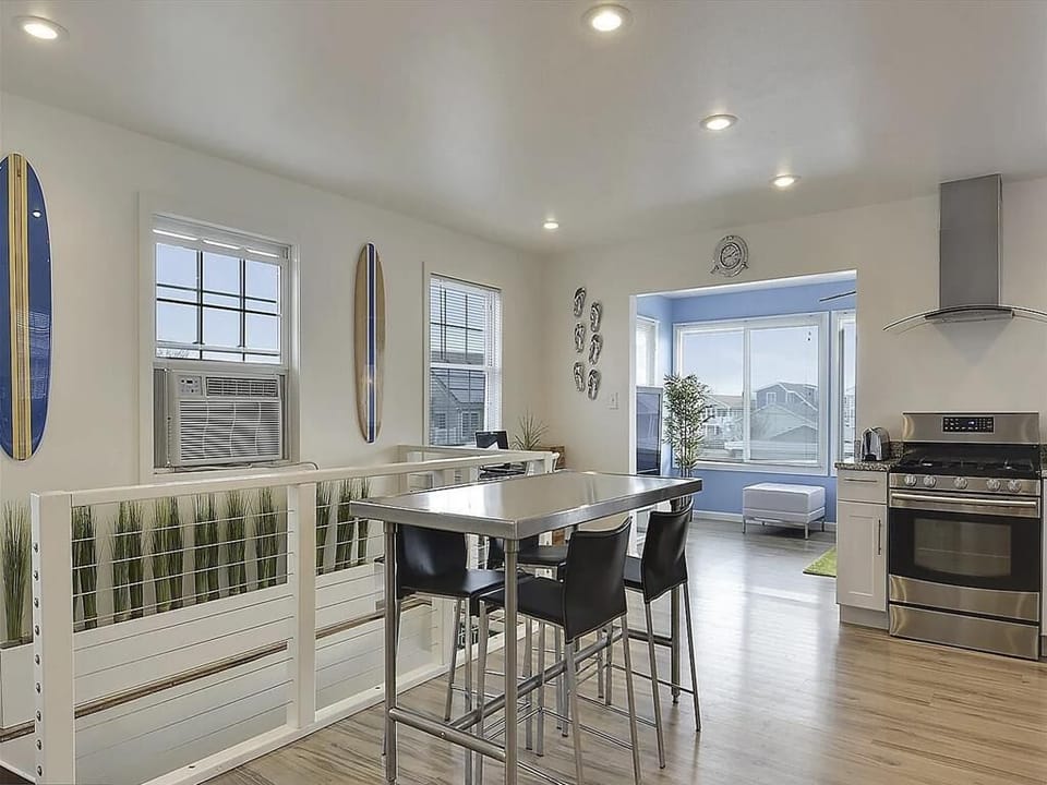 Modern kitchen with stainless steel gas range, dining table with bar stools, and surfboard wall décor.