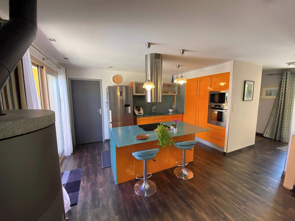 Cuisine américaine avec îlot central orange, tabourets de bar et parquet foncé
