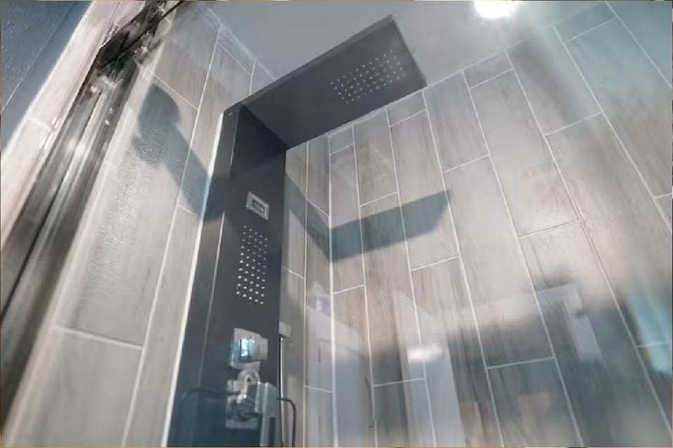 Close-up of modern shower interior with grey slate tiles, built-in wall niche shelf, chrome fixtures, and glass door.