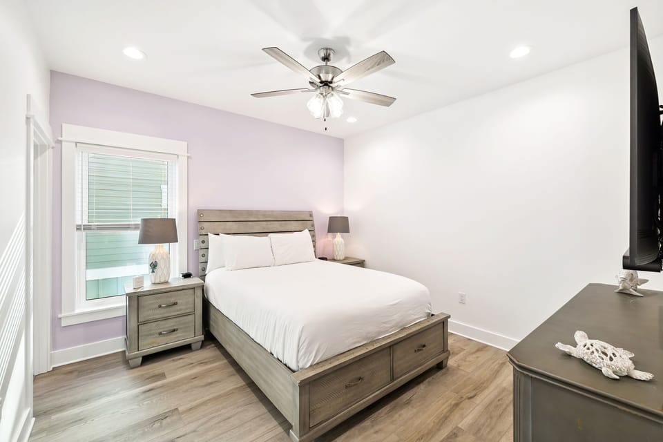 Drift off in your peaceful bedroom featuring a cozy queen bed, ceiling fan for comfort, and soft lavender walls that create a serene retreat.