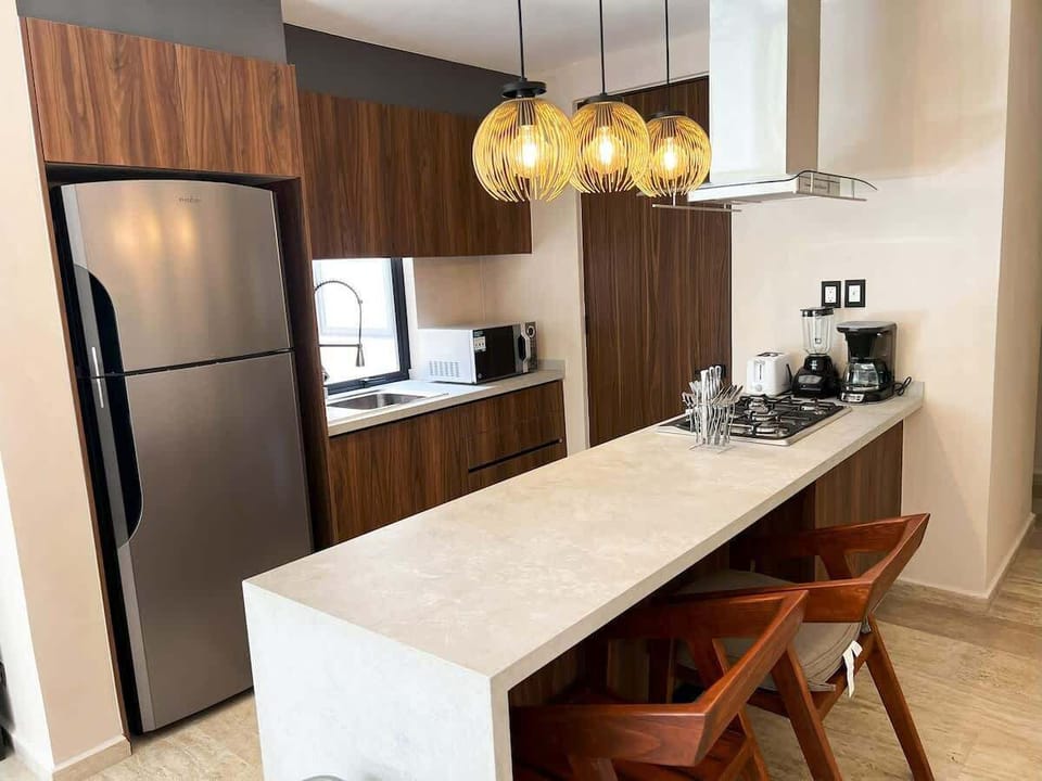 Cocina moderna totalmente equipada 
Cocina con barra desayunadora, refrigerador grande, electrodomésticos de acero inoxidable y lámparas colgantes de diseño elegante.