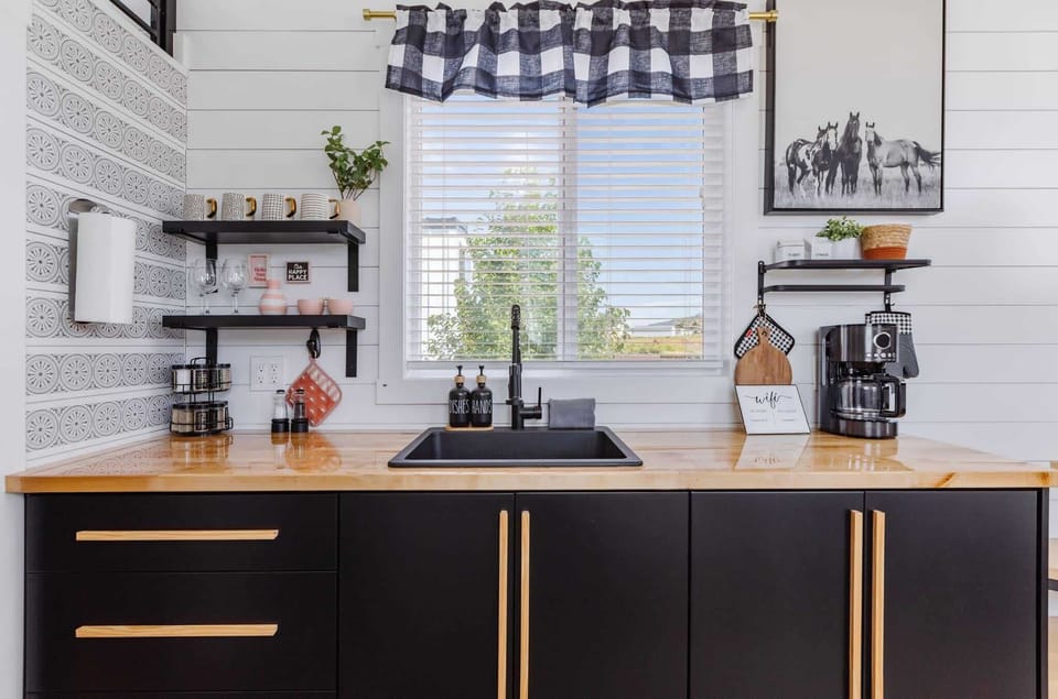 Stylish kitchen with modern black cabinetry, open shelving, coffee maker, and butcher block countertops. Bright windows and thoughtful details create a warm, functional space for cooking and relaxing during your stay.
