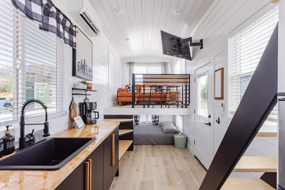 Open-concept tiny home with modern kitchen, loft bedroom, smart TV, and stylish living area. Bright white interior, large windows, and thoughtful design create a comfortable and inviting Southern Utah getaway.