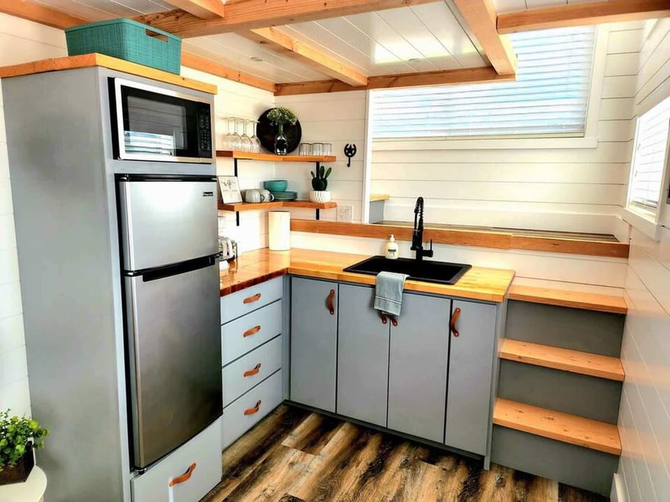 Compact, fully equipped kitchen featuring cooktop, sink, coffee maker, cookware, and open shelving. Thoughtfully designed for easy meal prep, morning coffee, and keeping everything organized during your stay.