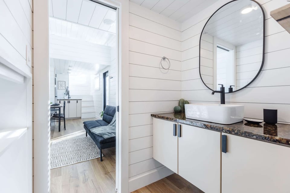 A separate vanity area with modern lighting, granite counters, and a stylish vessel sink creates extra space to get ready comfortably. Clean lines and bright finishes make this tiny home bathroom feel open and inviting.