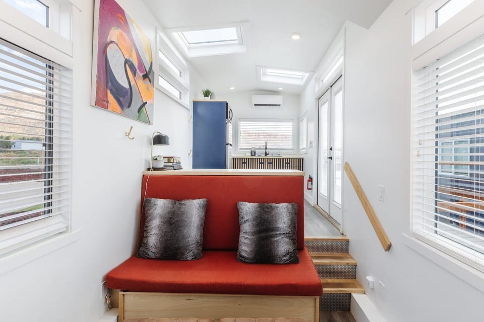 Built-in seating with comfortable cushions offers a relaxing place to unwind, enjoy a morning coffee, or take in the bright and airy feel of this modern tiny home.