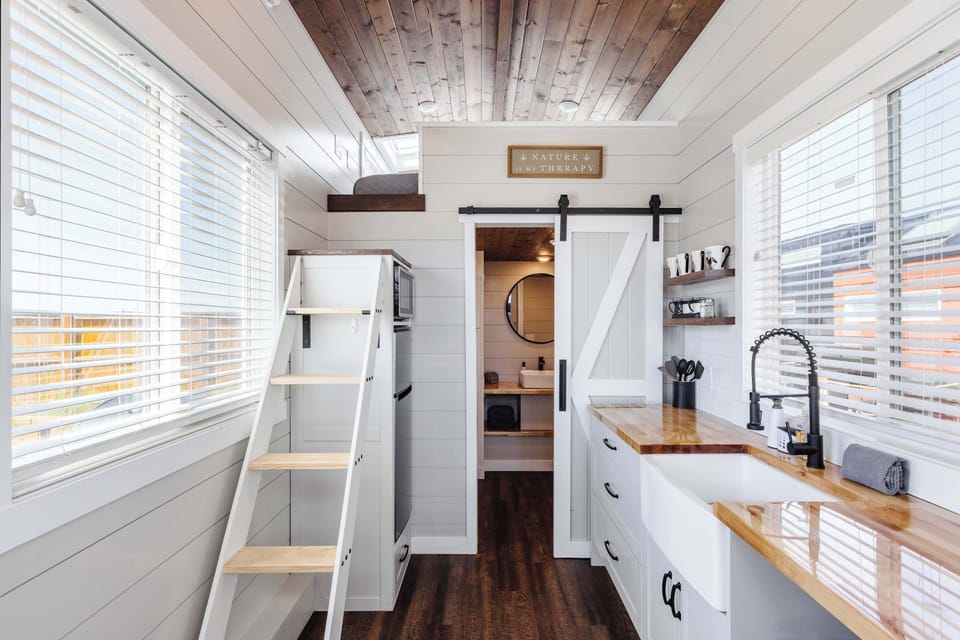 Well-equipped tiny home kitchen with refrigerator, microwave, ample storage, and convenient stairs leading to the loft.