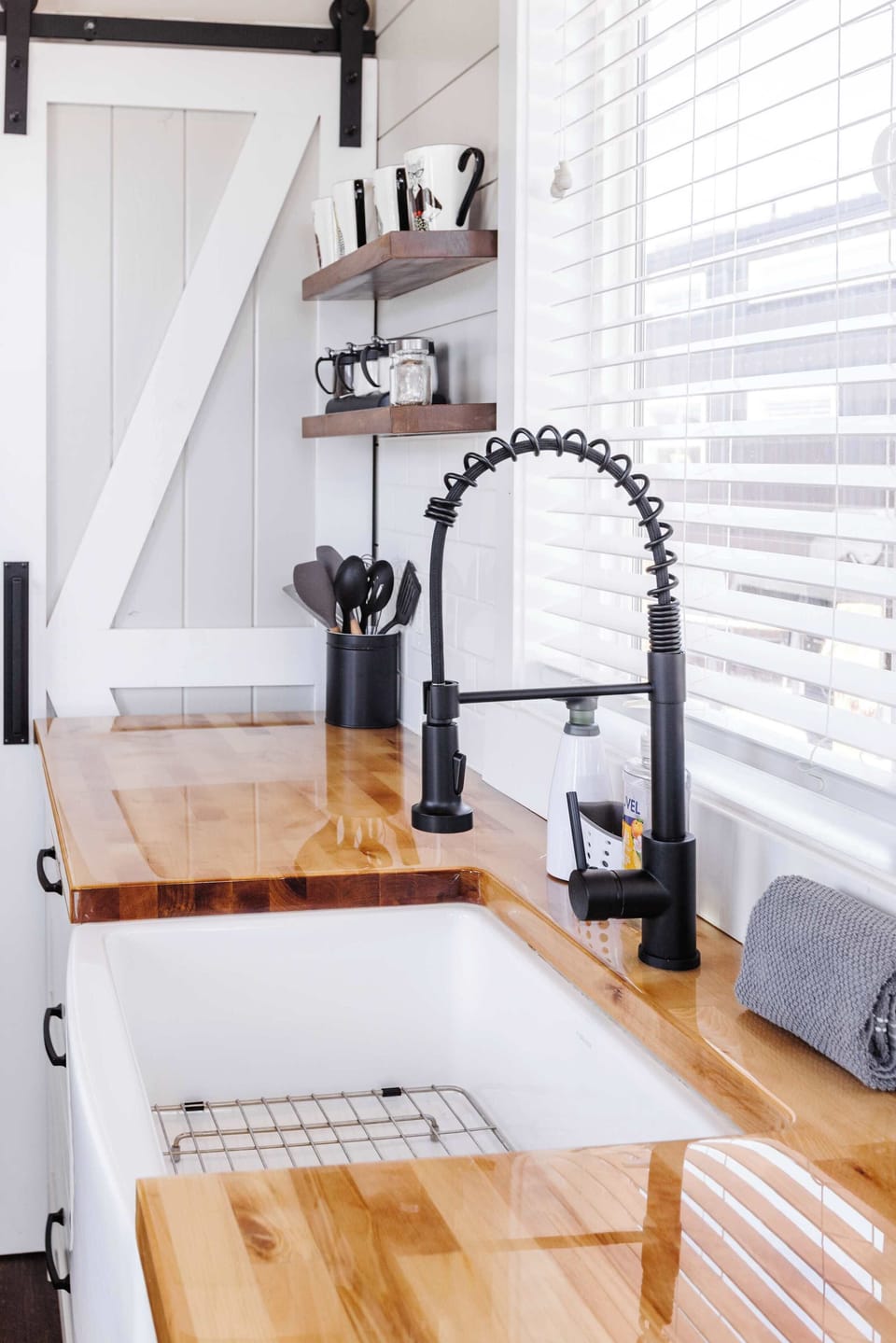 Close-up of the spacious farmhouse sink, modern pull-down faucet, cooking utensils, and open kitchen shelving.
