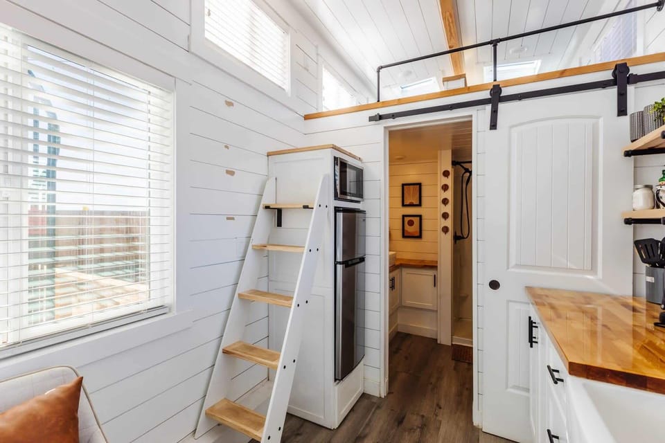 Modern tiny home kitchen with refrigerator and freezer, microwave, and cooktop. Open layout connects seamlessly to the loft sleeping area and cozy living space.