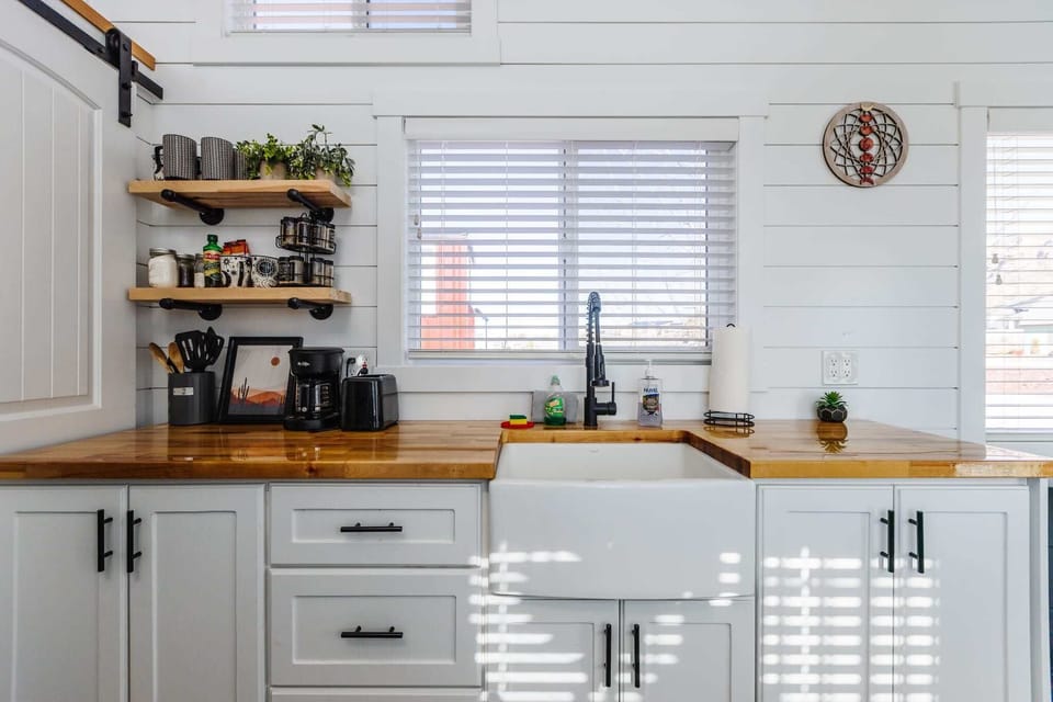 Spacious farmhouse sink beneath a bright window with butcher block countertops and ample prep space. Functional layout designed for comfort and convenience.