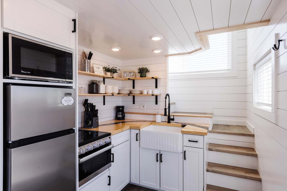 Light-filled kitchen with farmhouse sink and compact layout, showcasing the clever use of space inside this tiny home.