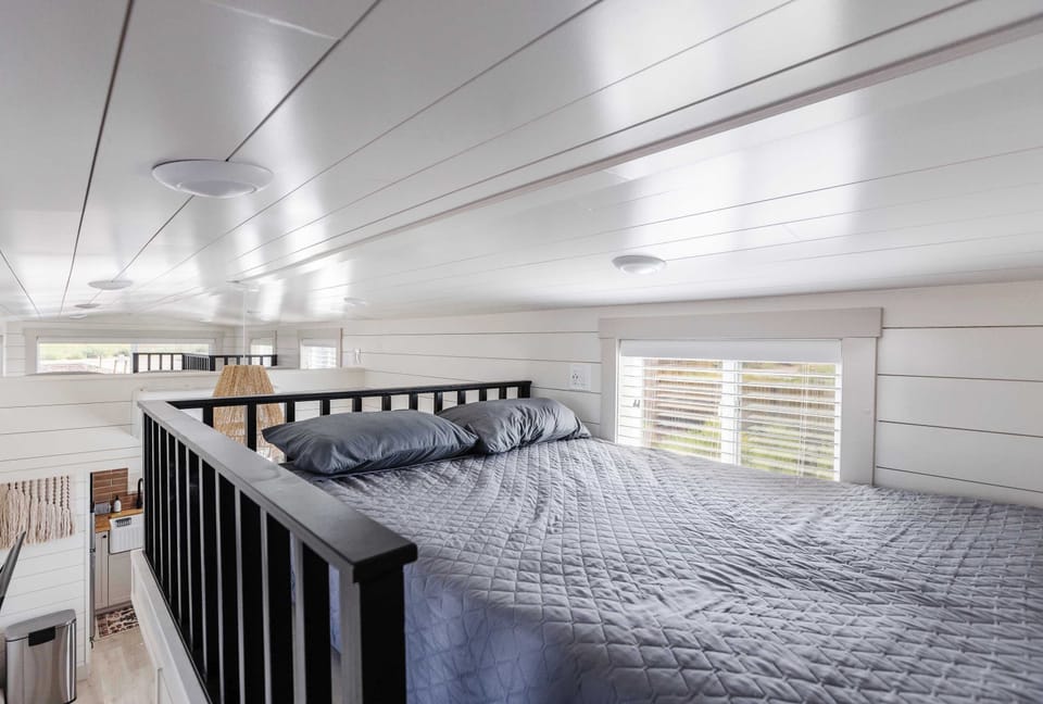 Bright loft bedroom with two double beds, multiple windows, and an open railing, offering additional sleeping space in this tiny home near Zion National Park.