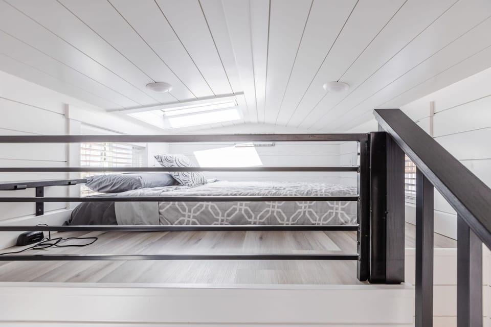 Loft with a queen bed and safety railing, showing the open connection to the living space below.